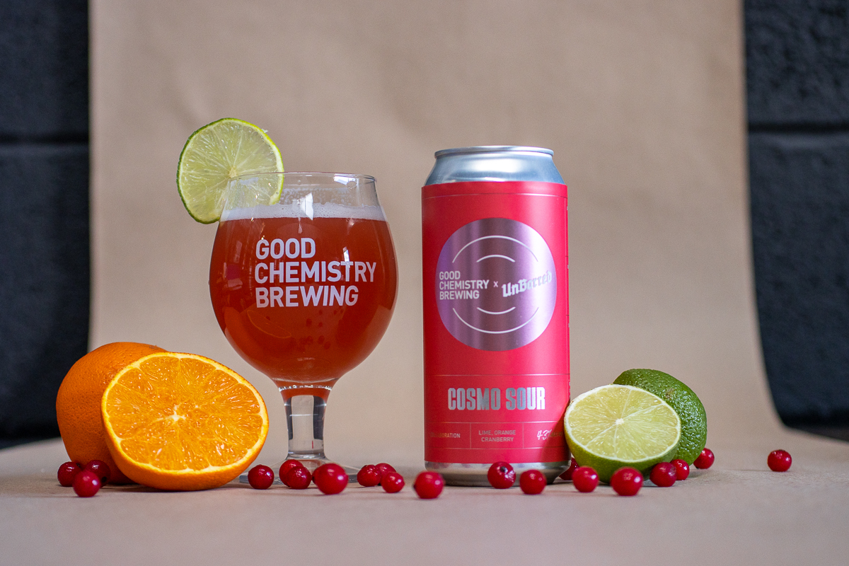Glass of beer and can of beer surrounded by limes, oranges and cranberries